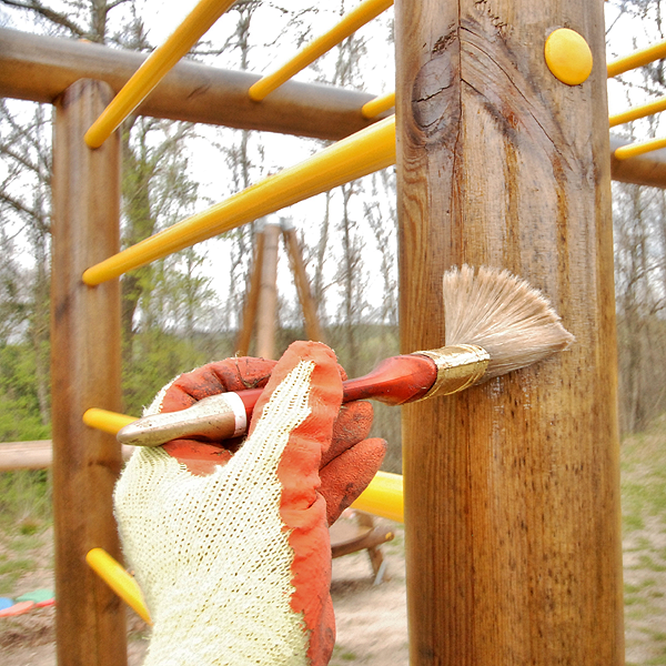 Close-up view of a gloved hand waterproofing a wooden support on playground equipment