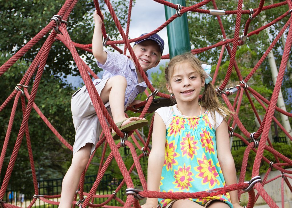 Two smiling children climbing on playground netting