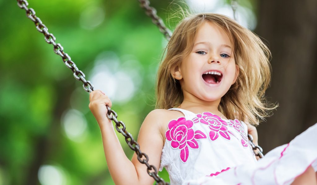 A smiling child swinging on a playground swing