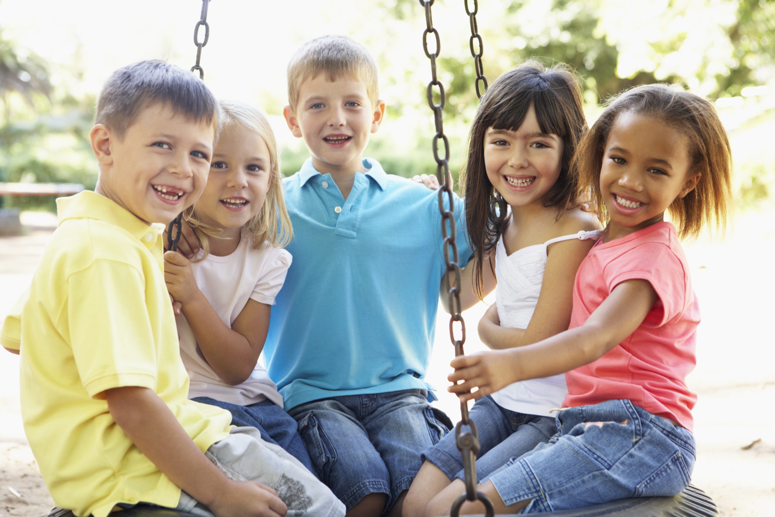Five smiling children sitting together in a tire swing on a playground